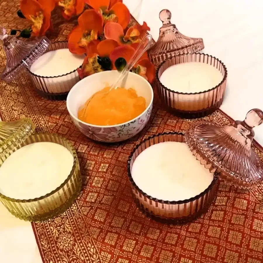 Bowls of exfoliating body scrub and scented candles on a traditional Thai patterned table runner