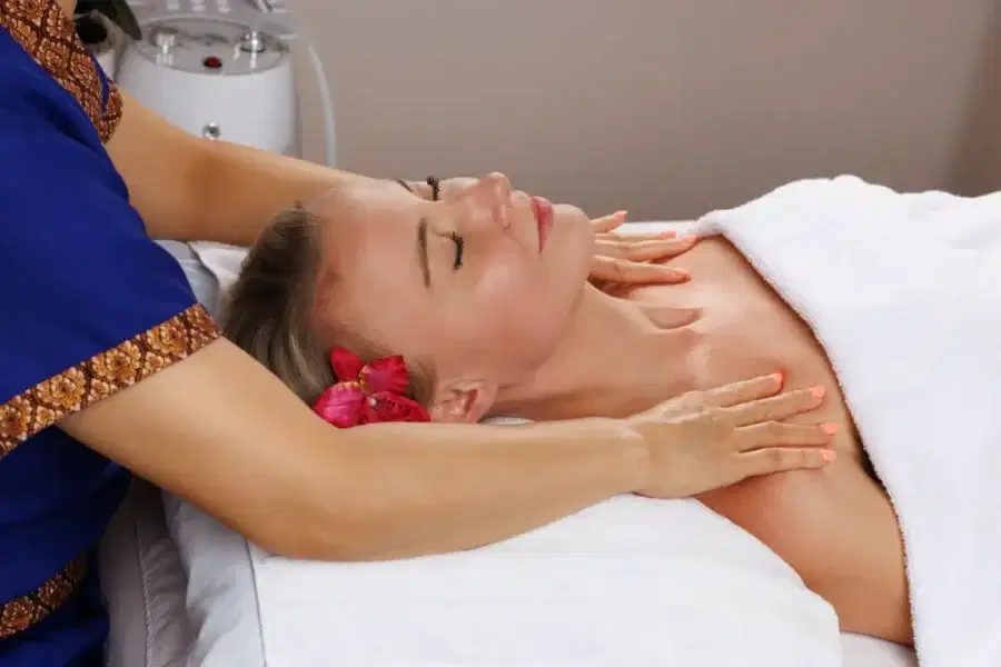 A woman with her eyes closed receiving a gentle neck and chest massage during a facial service